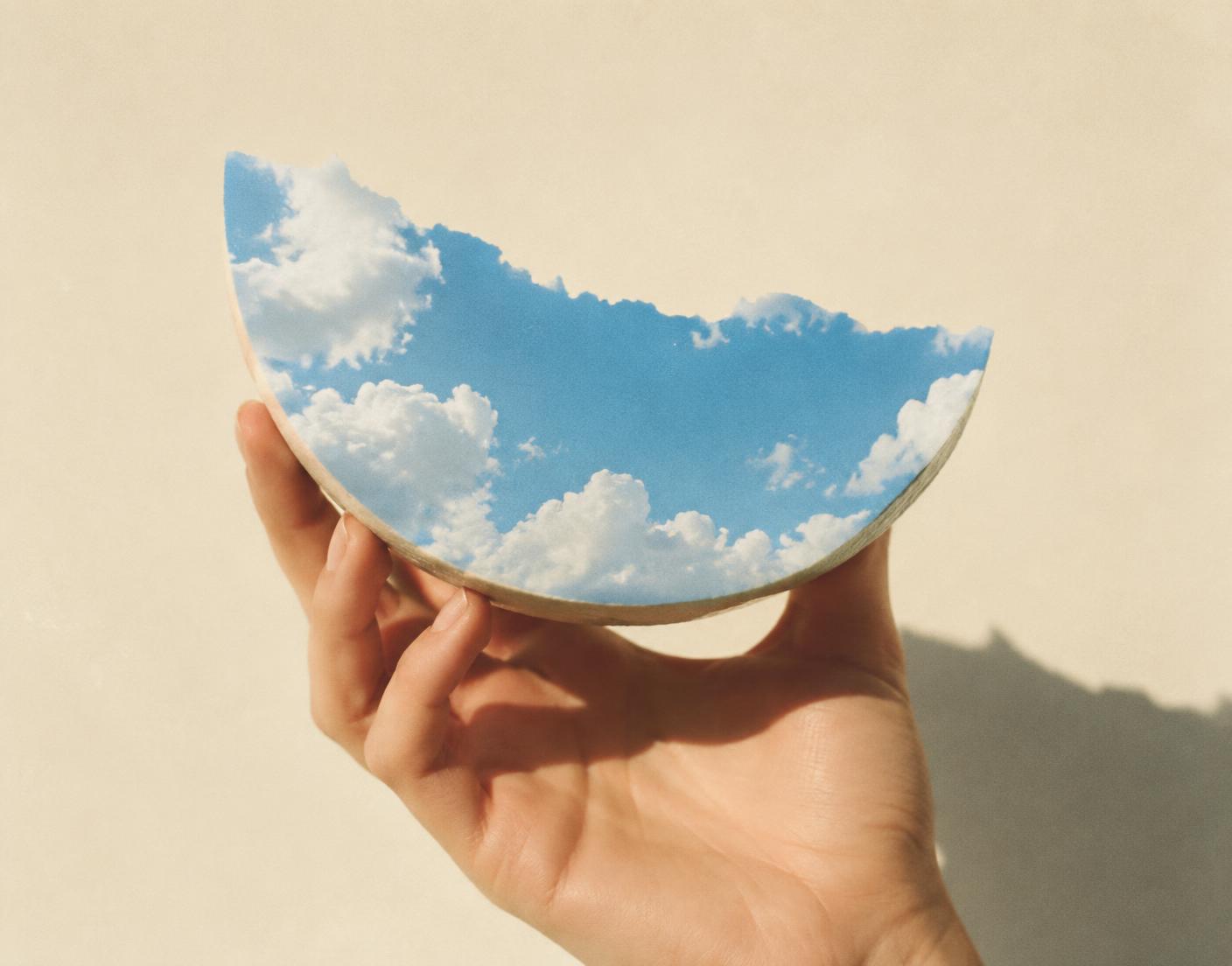 A hand holding a slice of sky as if it were fruit